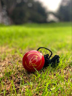 Red cricket ball with black stitches on grass